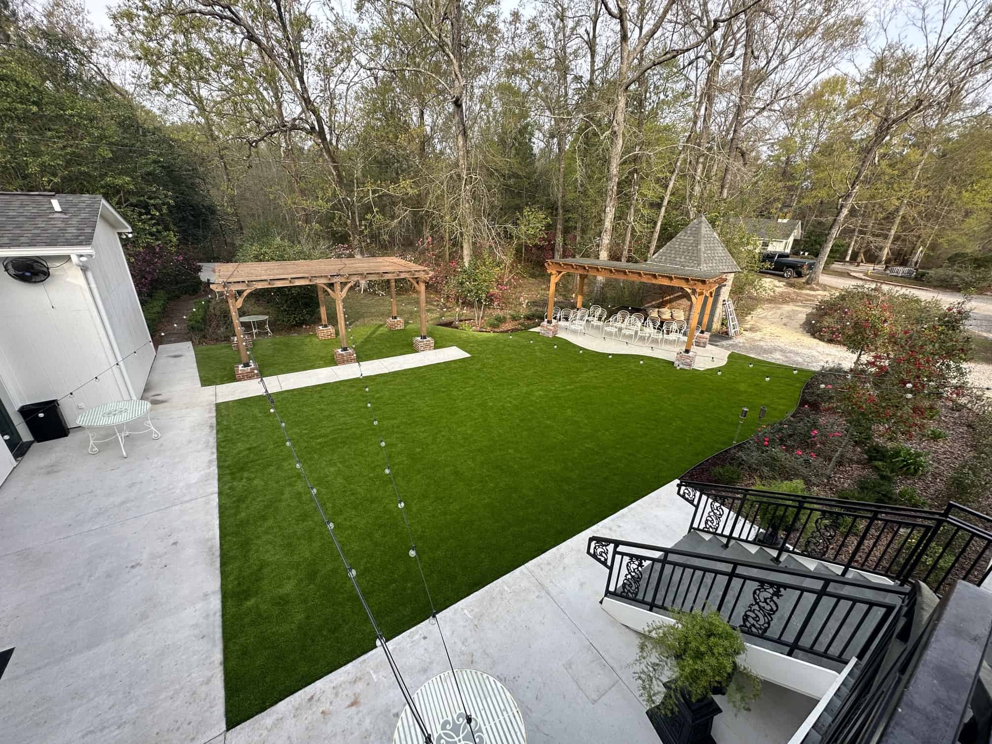 a backyard with two white pergolas, string lights, and bright green artificial turf